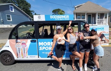 Four happy circuit riders pose in front of a BodyArmor branded circuit vehicle