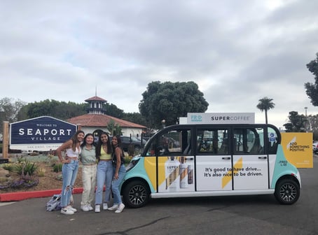 Four women smiling with a Super Coffee branded circuit vehicle in Seaport San Diego