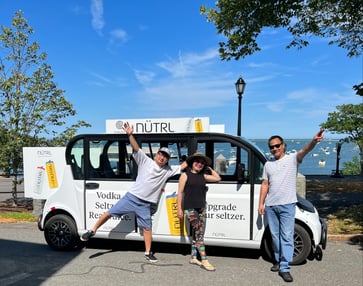 Three happy Circuit riders pose in front of a Nutrl-branded Circuit car