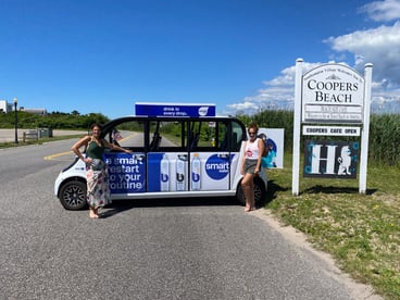 Two happy circuit riders pose with a Smartwater-branded Circuit car at Coopers Beach Southampton